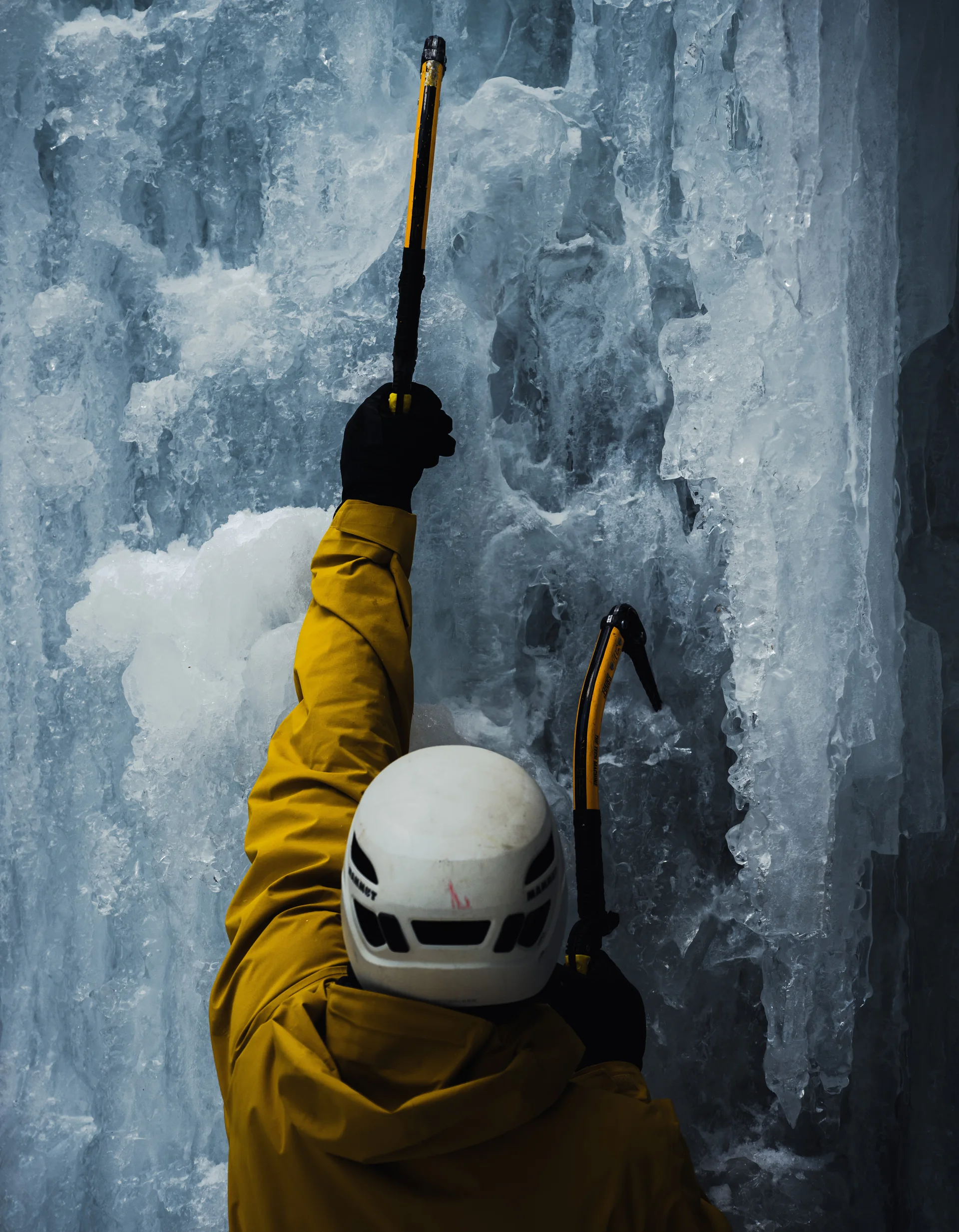 Ice climber in a yellow jacket against blue ice